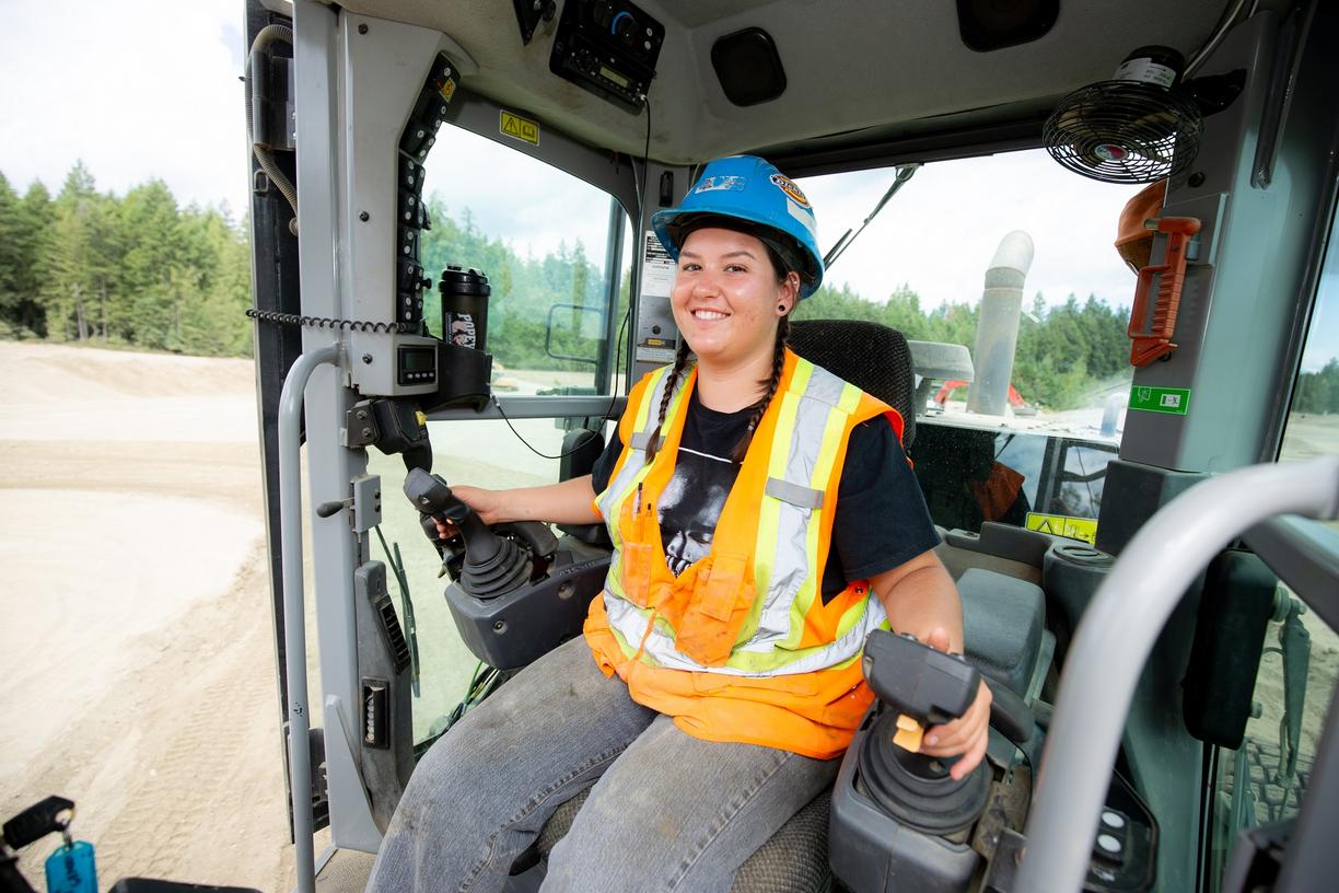 Smiling female student in a hard hat sitting in the cab of an excavator